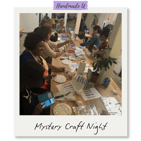 People gathered around a long table at a Mystery Craft Night event, working on crafts with 'Handmade U' branding